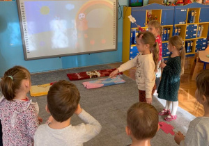Choreoterapia w grupie 1. Dzieci odtwarzają układ taneczny prezentowany na tablicy multimedialnej.